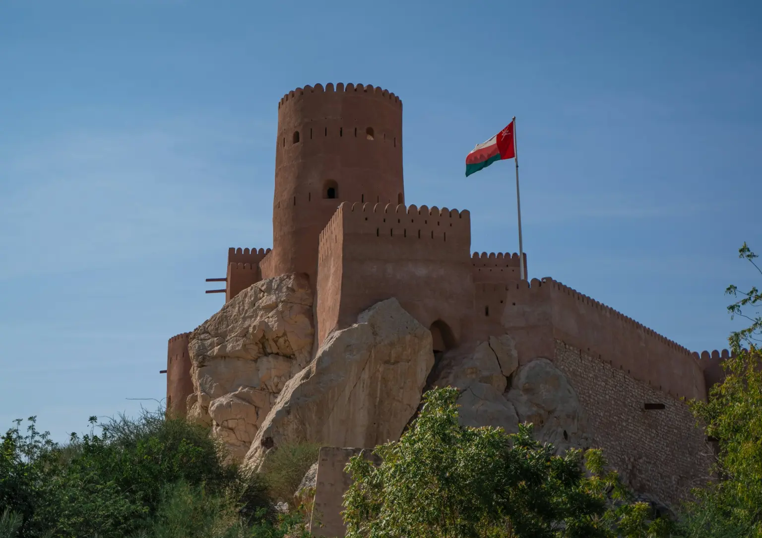 Omani hill fort with the national flag above green hills