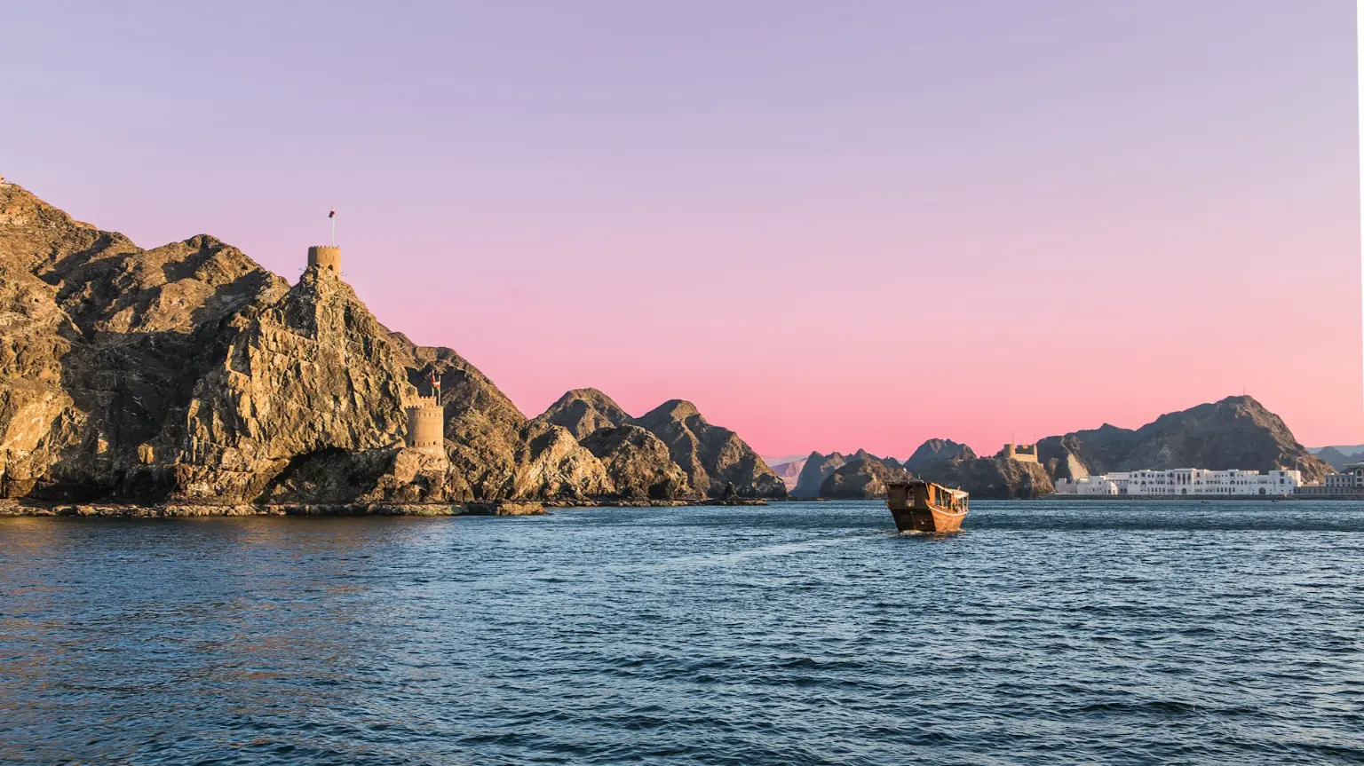 Traditional dhow on the Musandam coast beneath rugged cliffs at dusk